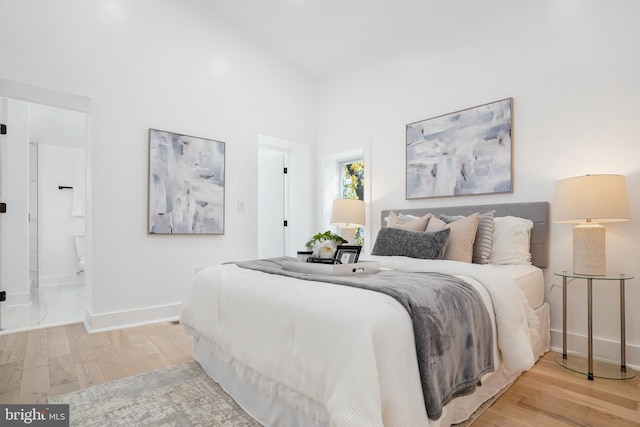 bedroom featuring ensuite bath, a towering ceiling, and light hardwood / wood-style flooring