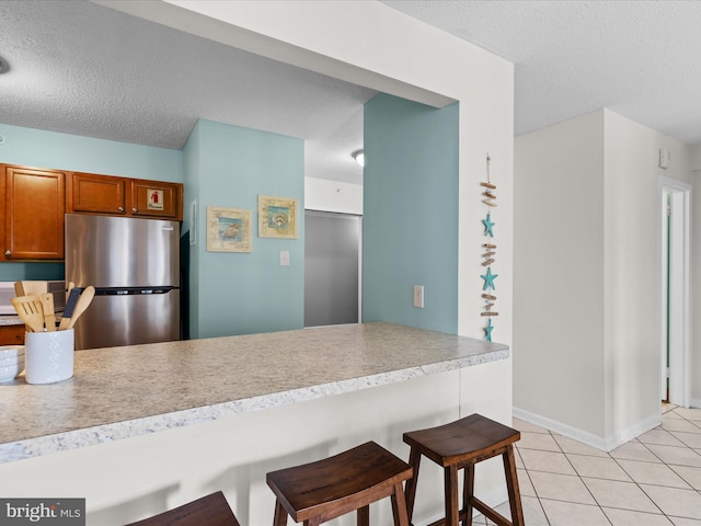 kitchen featuring a textured ceiling, stainless steel refrigerator, light tile patterned floors, a breakfast bar area, and kitchen peninsula