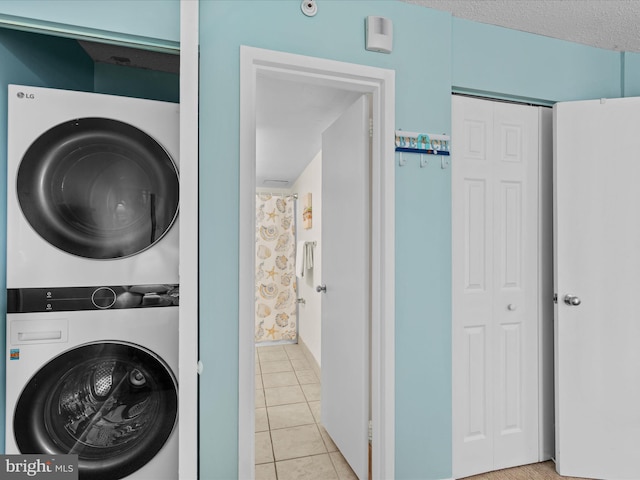 laundry room with a textured ceiling, light tile patterned floors, and stacked washer / dryer