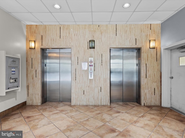 interior space with elevator, wooden walls, and a drop ceiling