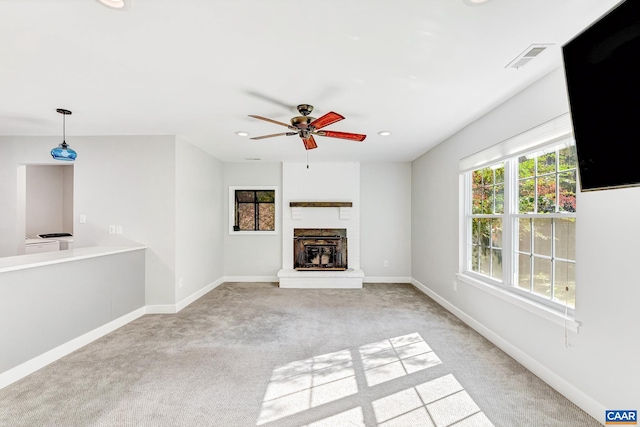 unfurnished living room featuring ceiling fan, a brick fireplace, and light colored carpet