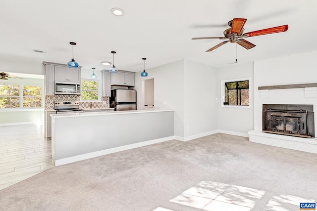 unfurnished living room featuring light carpet, a wealth of natural light, a brick fireplace, and ceiling fan