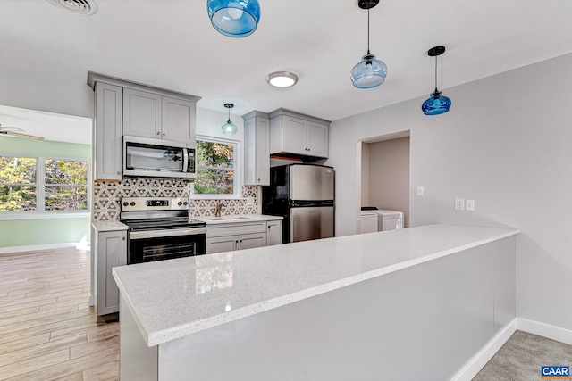 kitchen featuring light hardwood / wood-style flooring, appliances with stainless steel finishes, kitchen peninsula, and washing machine and dryer