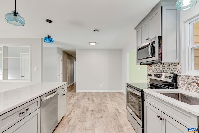 kitchen featuring backsplash, appliances with stainless steel finishes, light hardwood / wood-style flooring, pendant lighting, and sink