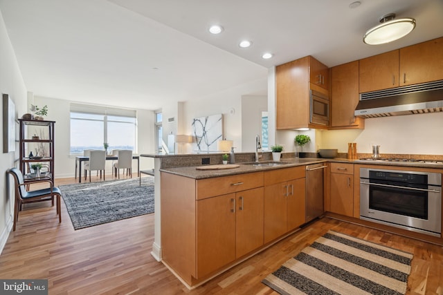 kitchen featuring kitchen peninsula, appliances with stainless steel finishes, sink, and light hardwood / wood-style flooring