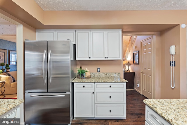 kitchen featuring dark wood-type flooring, light stone countertops, a textured ceiling, white cabinetry, and stainless steel refrigerator