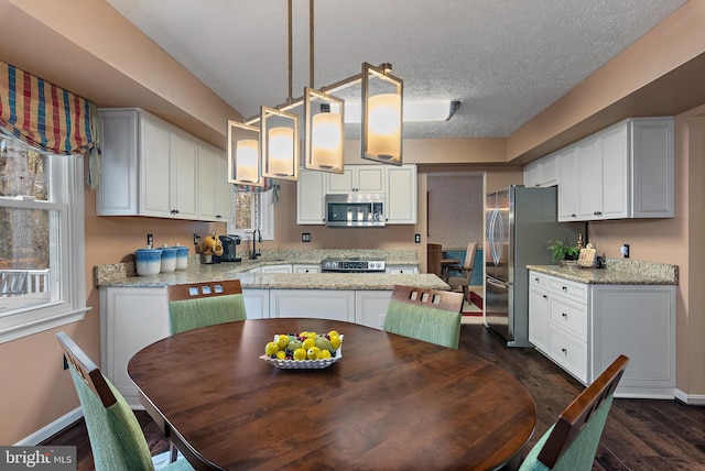 kitchen with hanging light fixtures, dark hardwood / wood-style floors, a textured ceiling, white cabinetry, and stainless steel appliances