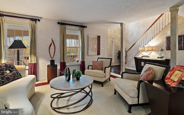 carpeted living room featuring ornate columns, a textured ceiling, and a wealth of natural light