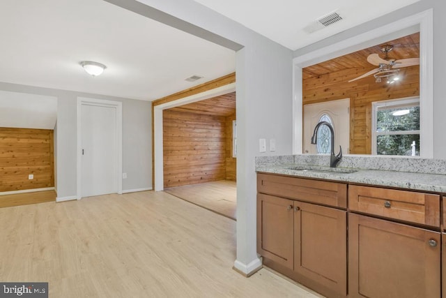 kitchen with light stone counters, wooden walls, sink, ceiling fan, and light wood-type flooring