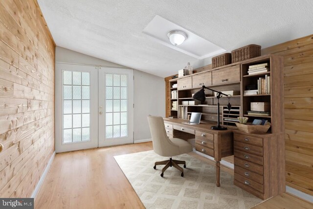 office featuring french doors, lofted ceiling, wood walls, a textured ceiling, and light hardwood / wood-style flooring