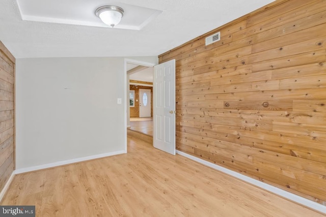 unfurnished room with light hardwood / wood-style flooring, wood walls, and vaulted ceiling