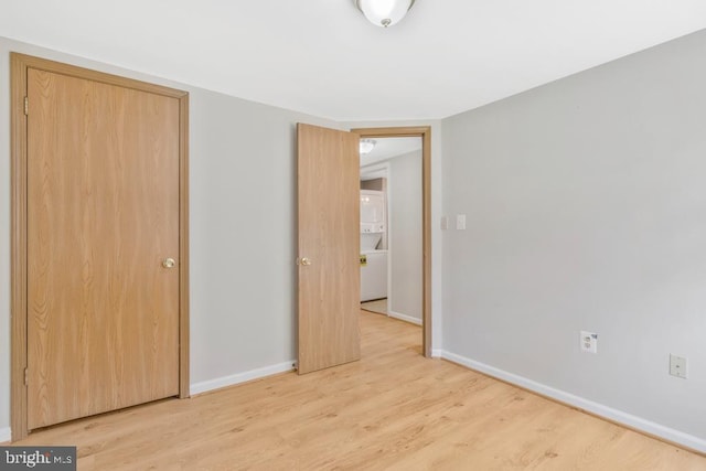 unfurnished bedroom featuring stacked washing maching and dryer, light hardwood / wood-style flooring, and a closet