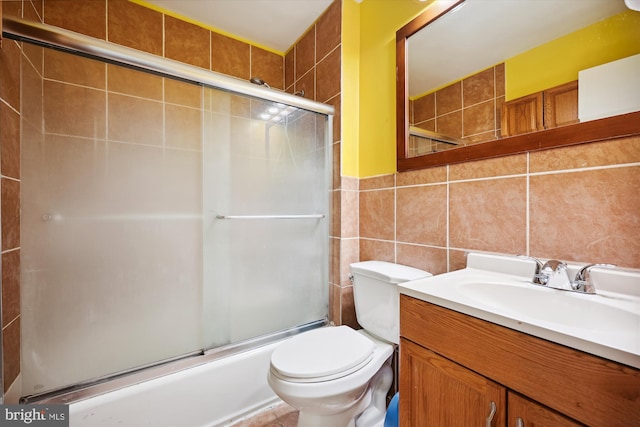 full bathroom featuring toilet, vanity, shower / bath combination with glass door, and tile walls