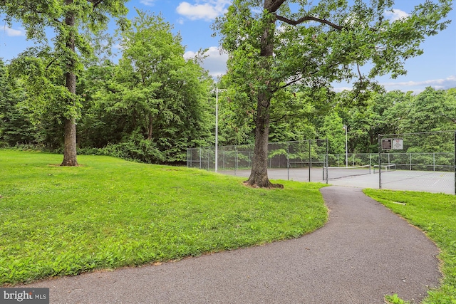 view of property's community with a lawn and tennis court