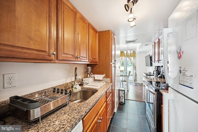 kitchen featuring stainless steel electric range oven, sink, dark tile patterned flooring, dark stone counters, and white fridge