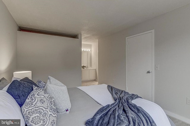 bedroom with ensuite bathroom, a textured ceiling, and carpet flooring