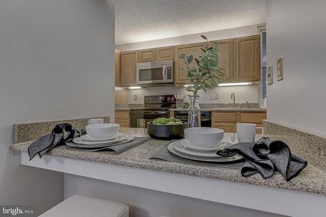 kitchen featuring sink, a breakfast bar area, a textured ceiling, kitchen peninsula, and black appliances