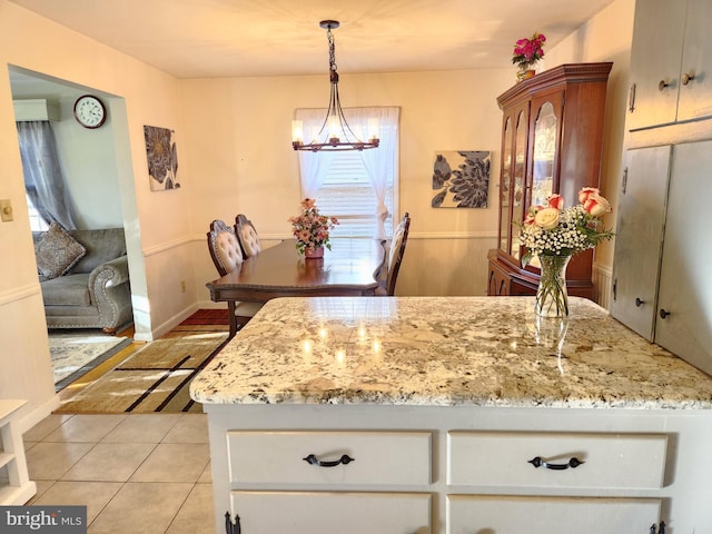 kitchen featuring hanging light fixtures, white cabinetry, light stone countertops, light tile patterned flooring, and a notable chandelier