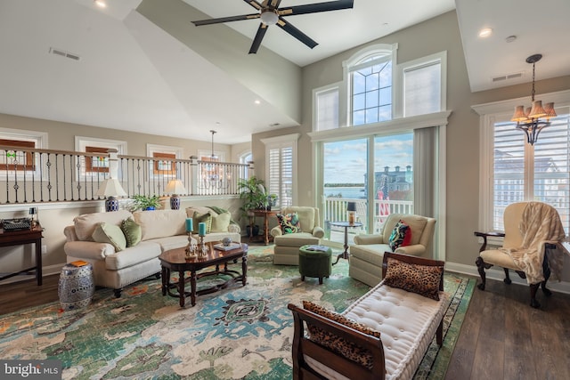 living room with ceiling fan with notable chandelier, dark hardwood / wood-style flooring, and a high ceiling