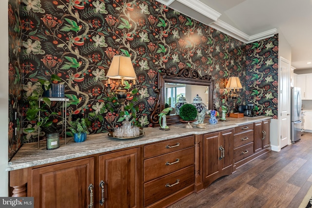 kitchen with dark hardwood / wood-style floors, light stone counters, ornamental molding, and stainless steel refrigerator