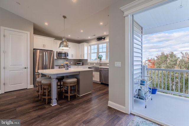 kitchen featuring stainless steel appliances, dark wood-type flooring, a center island, white cabinetry, and hanging light fixtures