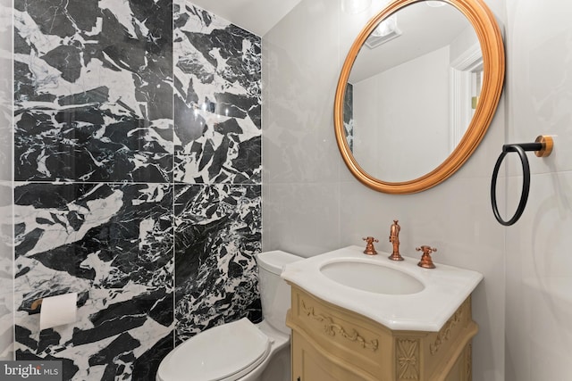 bathroom with toilet, vanity, and tile walls