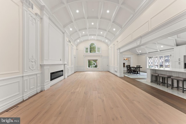 unfurnished living room featuring plenty of natural light, ornate columns, light wood-type flooring, and lofted ceiling