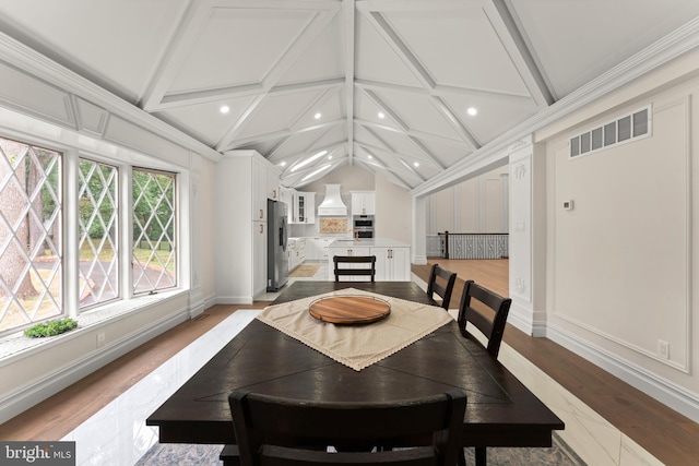 dining room featuring light wood-type flooring and vaulted ceiling with beams