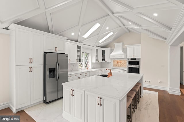 kitchen featuring stainless steel appliances, light stone countertops, white cabinets, custom exhaust hood, and a center island