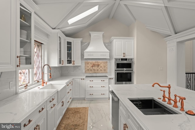 kitchen featuring appliances with stainless steel finishes, custom range hood, light stone countertops, sink, and lofted ceiling with skylight