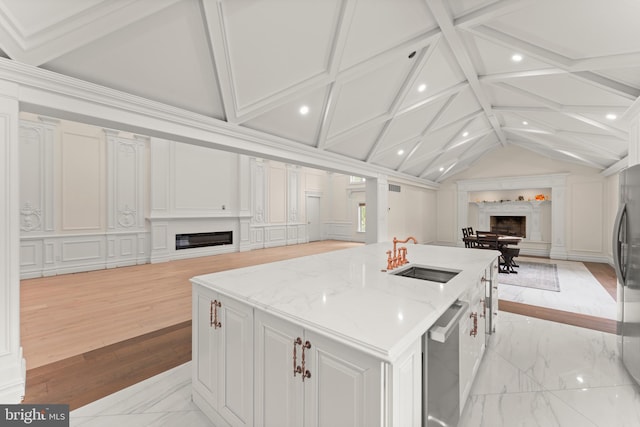 kitchen with a large island with sink, sink, light stone counters, vaulted ceiling with beams, and white cabinets