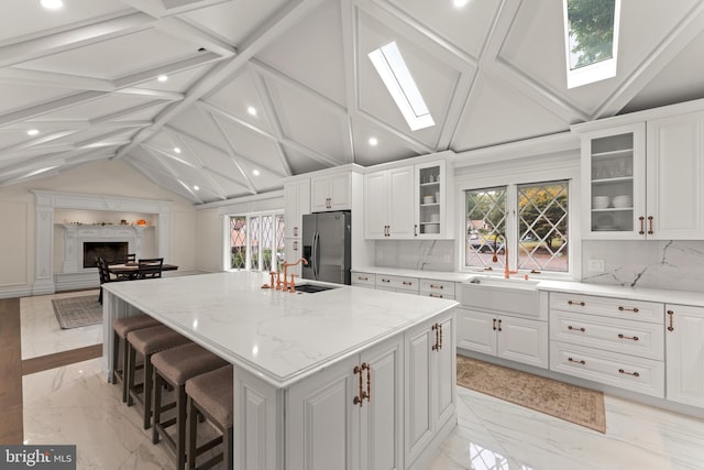 kitchen with vaulted ceiling with skylight, light stone counters, a center island with sink, stainless steel fridge with ice dispenser, and a wealth of natural light