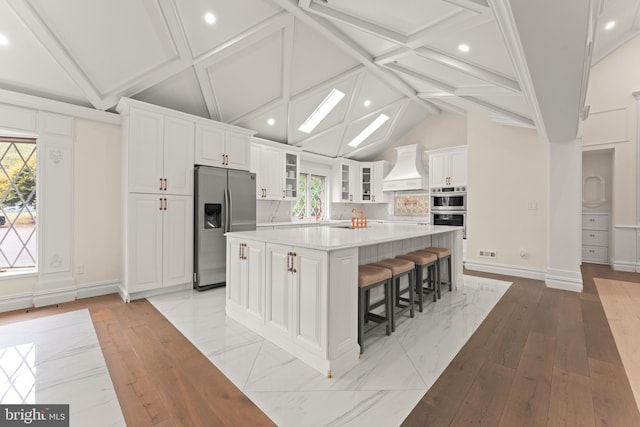 kitchen featuring stainless steel appliances, white cabinets, a breakfast bar, a spacious island, and lofted ceiling with beams