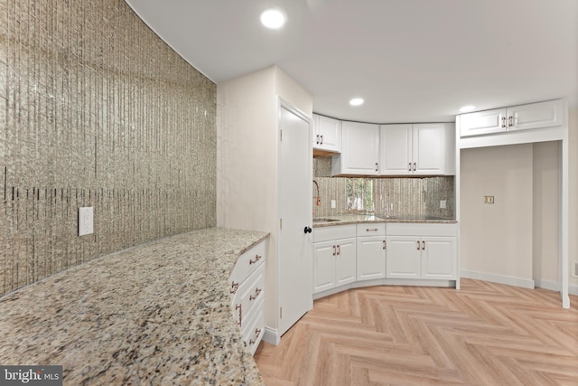 kitchen with light parquet floors, light stone countertops, sink, and white cabinets