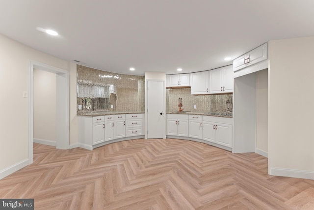 kitchen featuring backsplash, white cabinetry, light parquet floors, and light stone counters