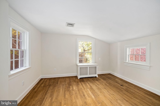 empty room featuring light hardwood / wood-style floors, lofted ceiling, radiator, and a wealth of natural light