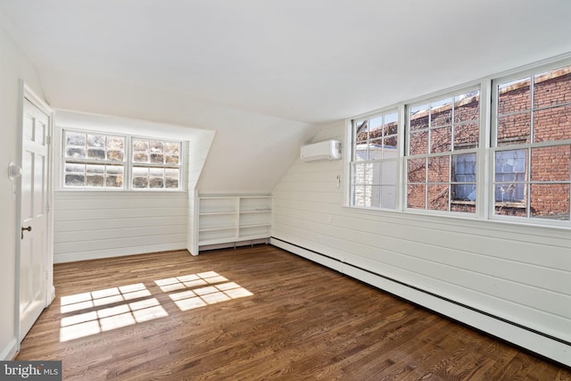 additional living space featuring lofted ceiling, a baseboard heating unit, a wall unit AC, and hardwood / wood-style flooring