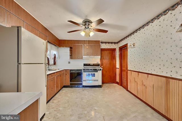 kitchen featuring white appliances, ceiling fan, sink, and wooden walls