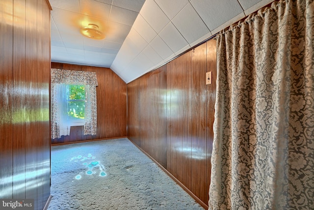 corridor with wood walls, carpet, and vaulted ceiling