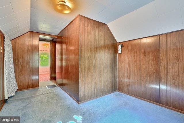 hallway with light carpet, wooden walls, and vaulted ceiling