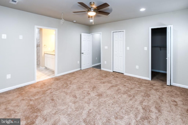 unfurnished bedroom featuring a walk in closet, ensuite bathroom, ceiling fan, and light carpet