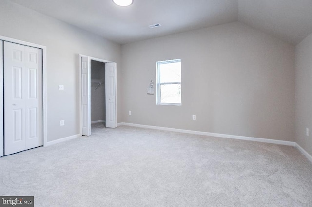 unfurnished bedroom featuring multiple closets, light colored carpet, and vaulted ceiling