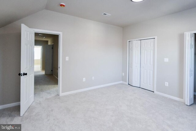 unfurnished bedroom featuring a closet, light carpet, and vaulted ceiling