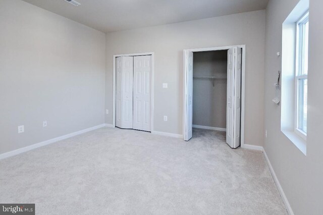 unfurnished bedroom featuring light carpet, multiple windows, and multiple closets