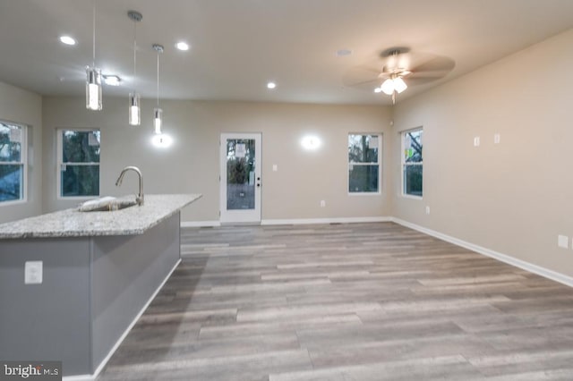 kitchen featuring light stone countertops, ceiling fan, a kitchen island with sink, sink, and hanging light fixtures