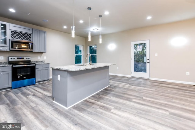 kitchen featuring gray cabinetry, sink, stainless steel appliances, an island with sink, and decorative light fixtures