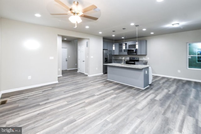 kitchen with light stone countertops, gray cabinetry, stainless steel appliances, a kitchen island with sink, and pendant lighting