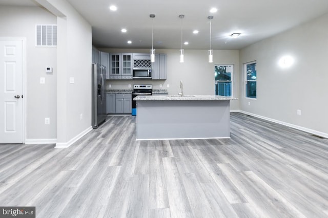 kitchen featuring light stone countertops, appliances with stainless steel finishes, decorative light fixtures, gray cabinets, and an island with sink