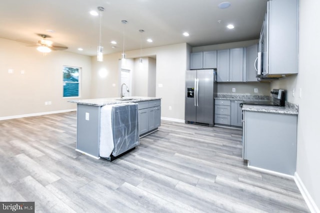 kitchen featuring sink, an island with sink, appliances with stainless steel finishes, decorative light fixtures, and light stone counters