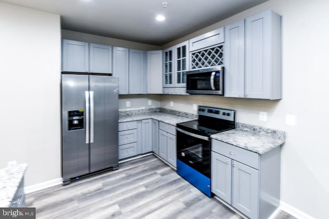 kitchen featuring gray cabinetry, light hardwood / wood-style floors, light stone countertops, and stainless steel appliances